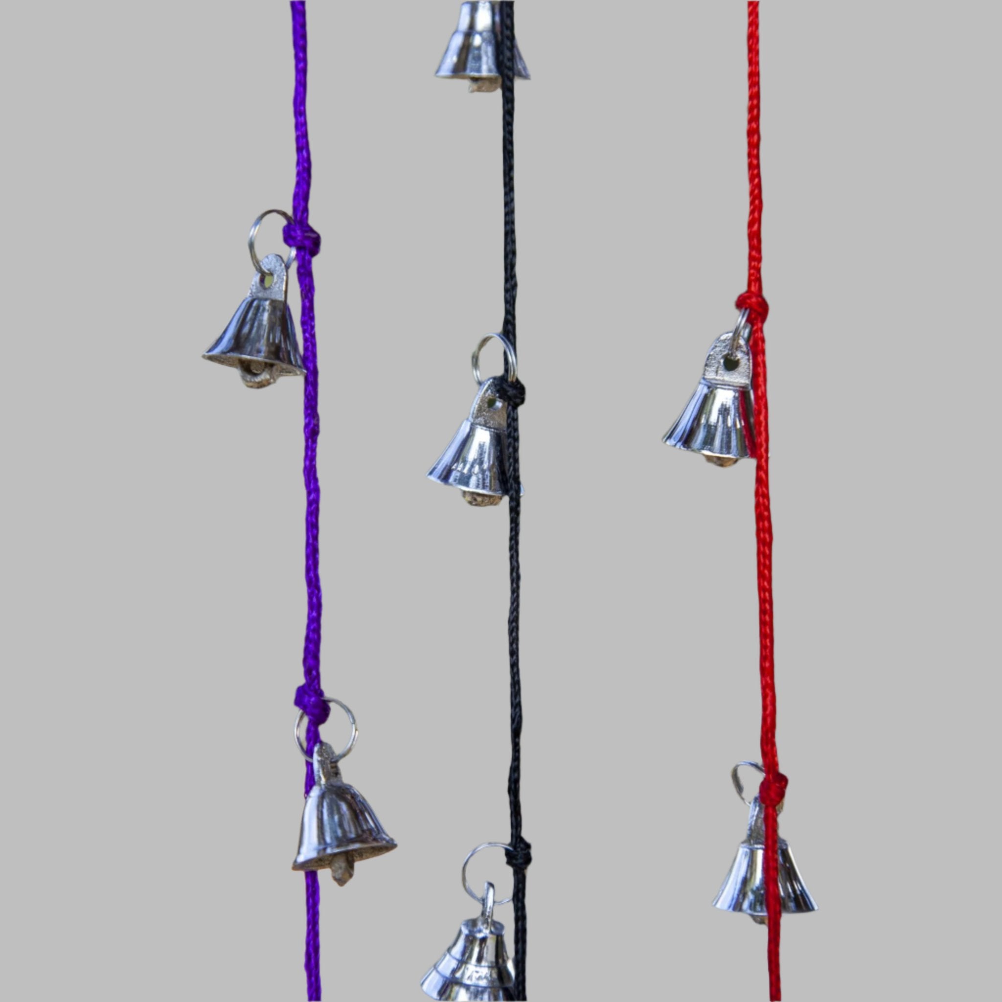 Strands of small silver tone brass bells hanging on green purple black and red cords, each cord about 30 inches long.
