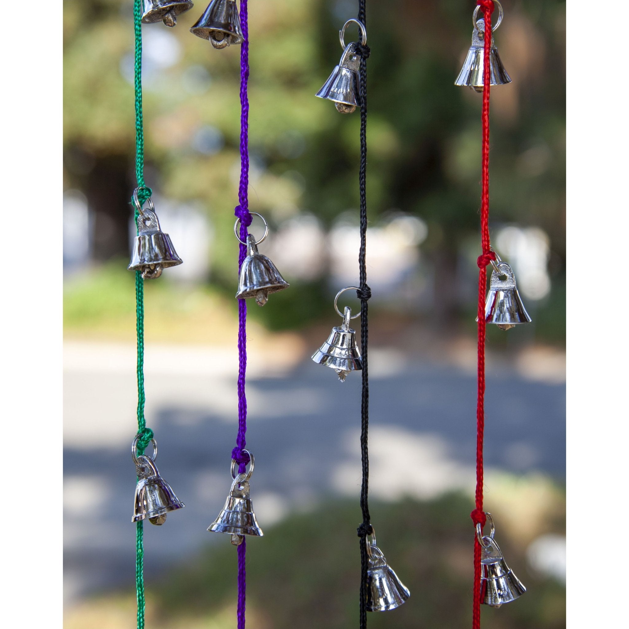 Strands of small silver tone brass bells hanging on green purple black and red cords, each cord about 30 inches long.