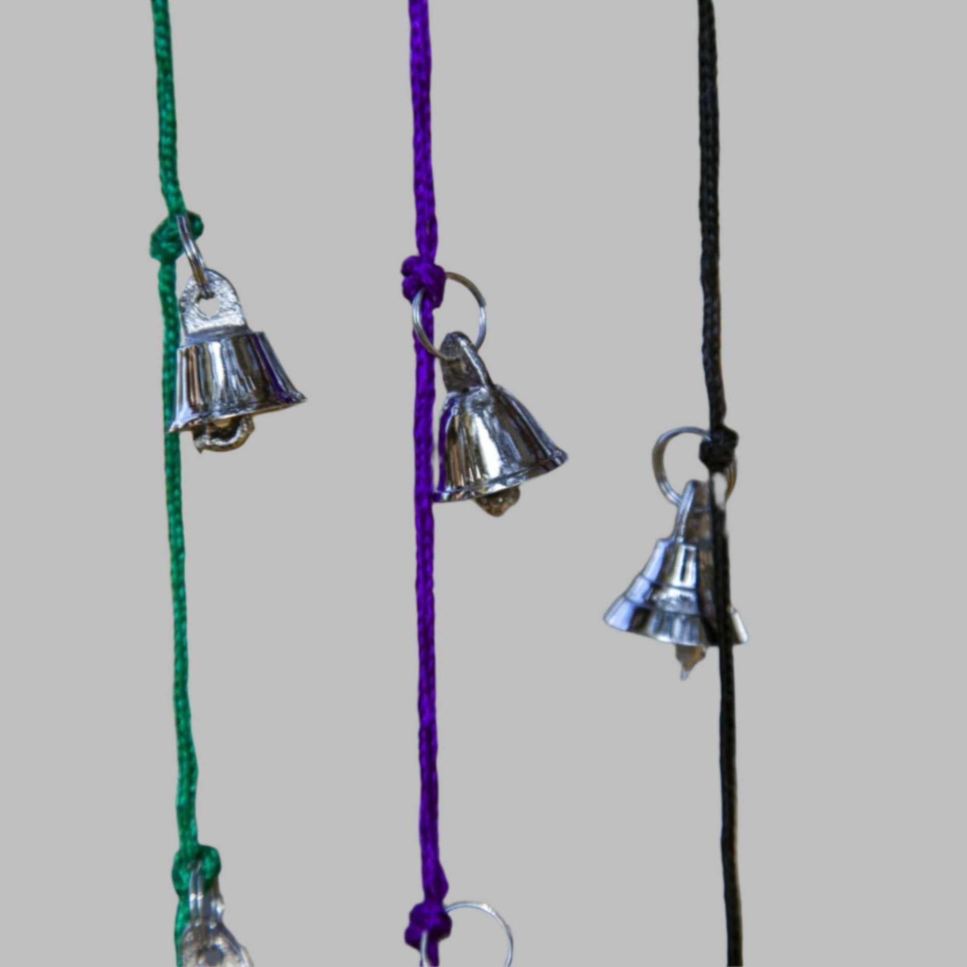 Strands of small silver tone brass bells hanging on green purple black and red cords, each cord about 30 inches long.